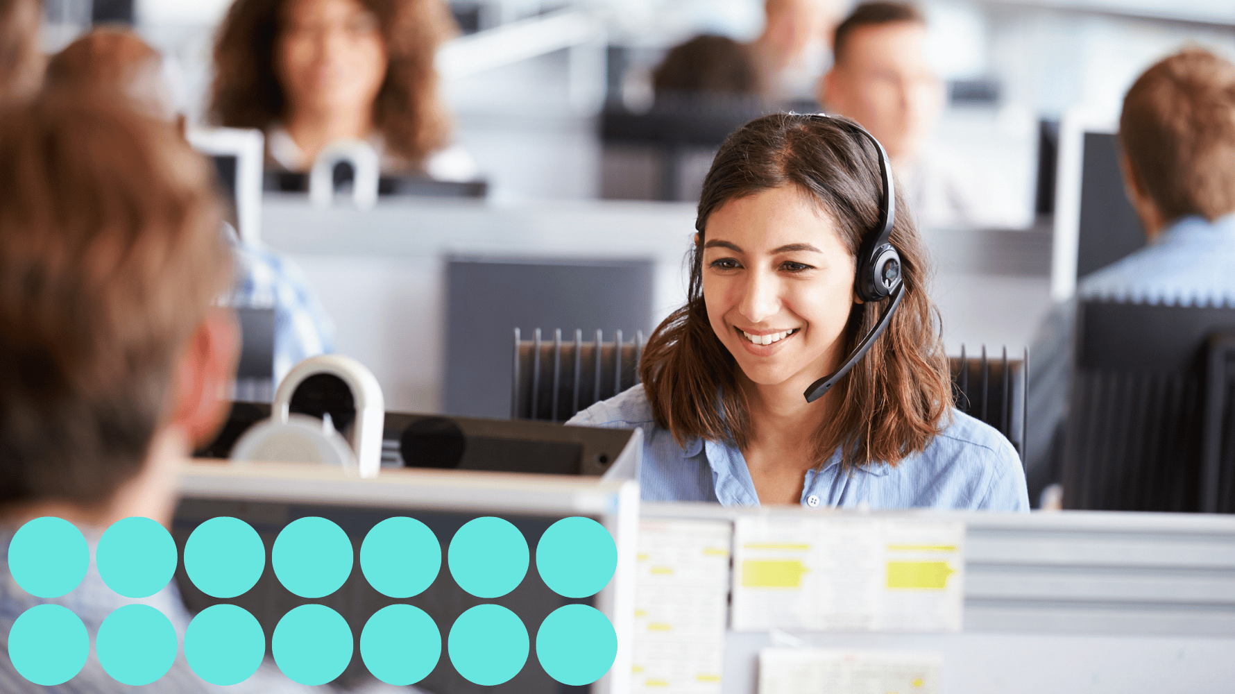 A room filled with people sitting down at desks wearing headsets. Fourteen blue graphic circles are in the lower lefthand corner of the image.