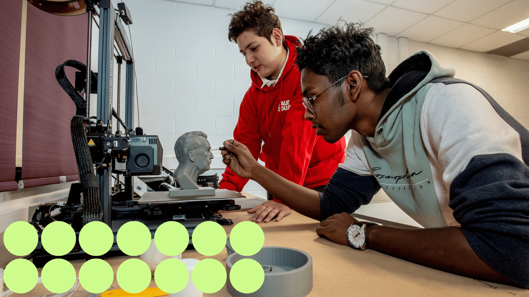 Two students are working on an animated related project at a table. Fourteen green graphic circles are in the lower lefthand corner of the image.