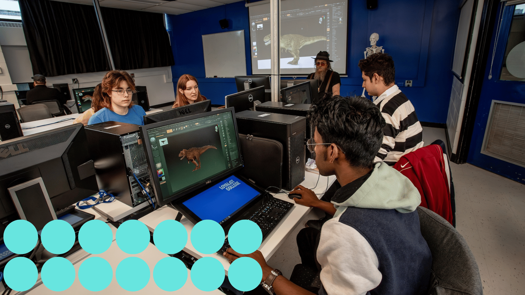 A group of students are sitting down inside a computer lab. A professor is sitting in front of the classroom with a display behind showing the lecture for animation and game development related studies. Fourteen blue graphic circles are in the lower lefthand corner of the image.