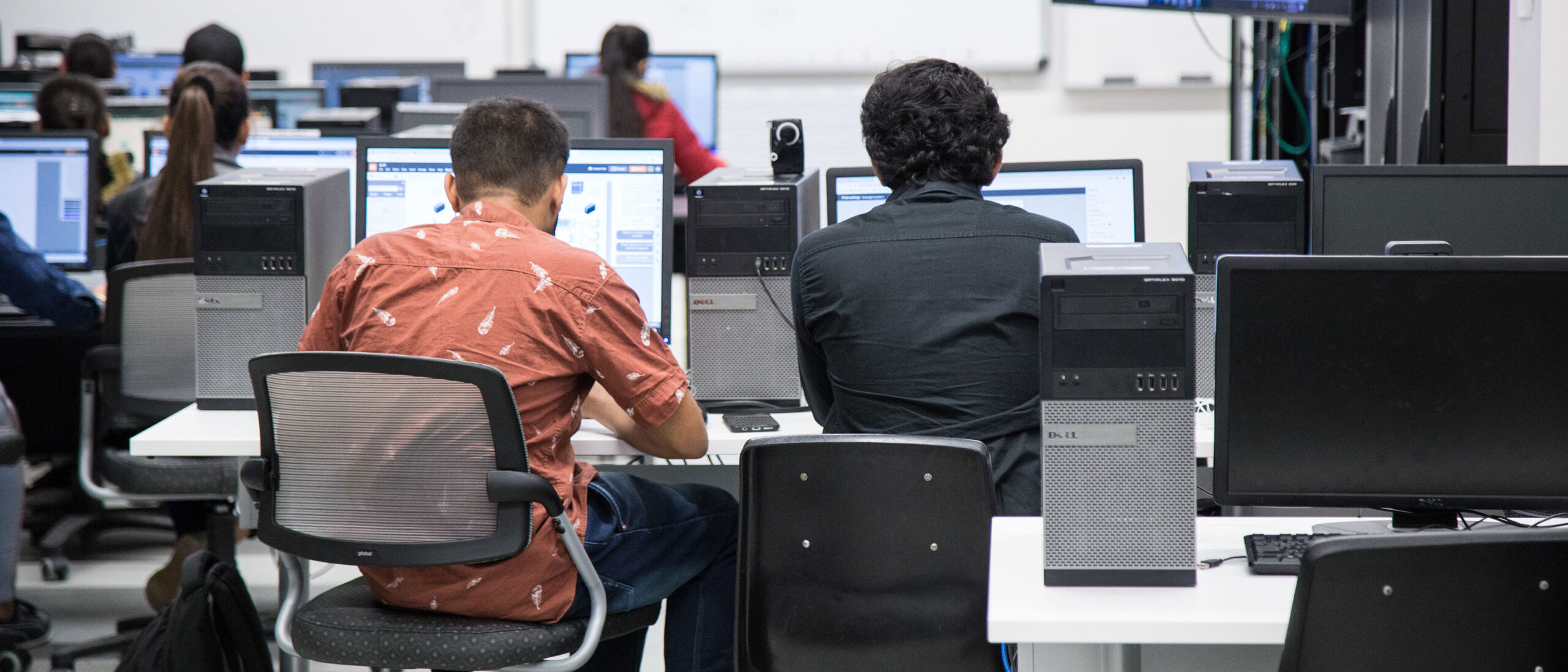 Students in the Computer Systems Technician program at Loyalist College are working on computers in a computer lab. The students are focused on their screens, engaging in various technical tasks and projects.