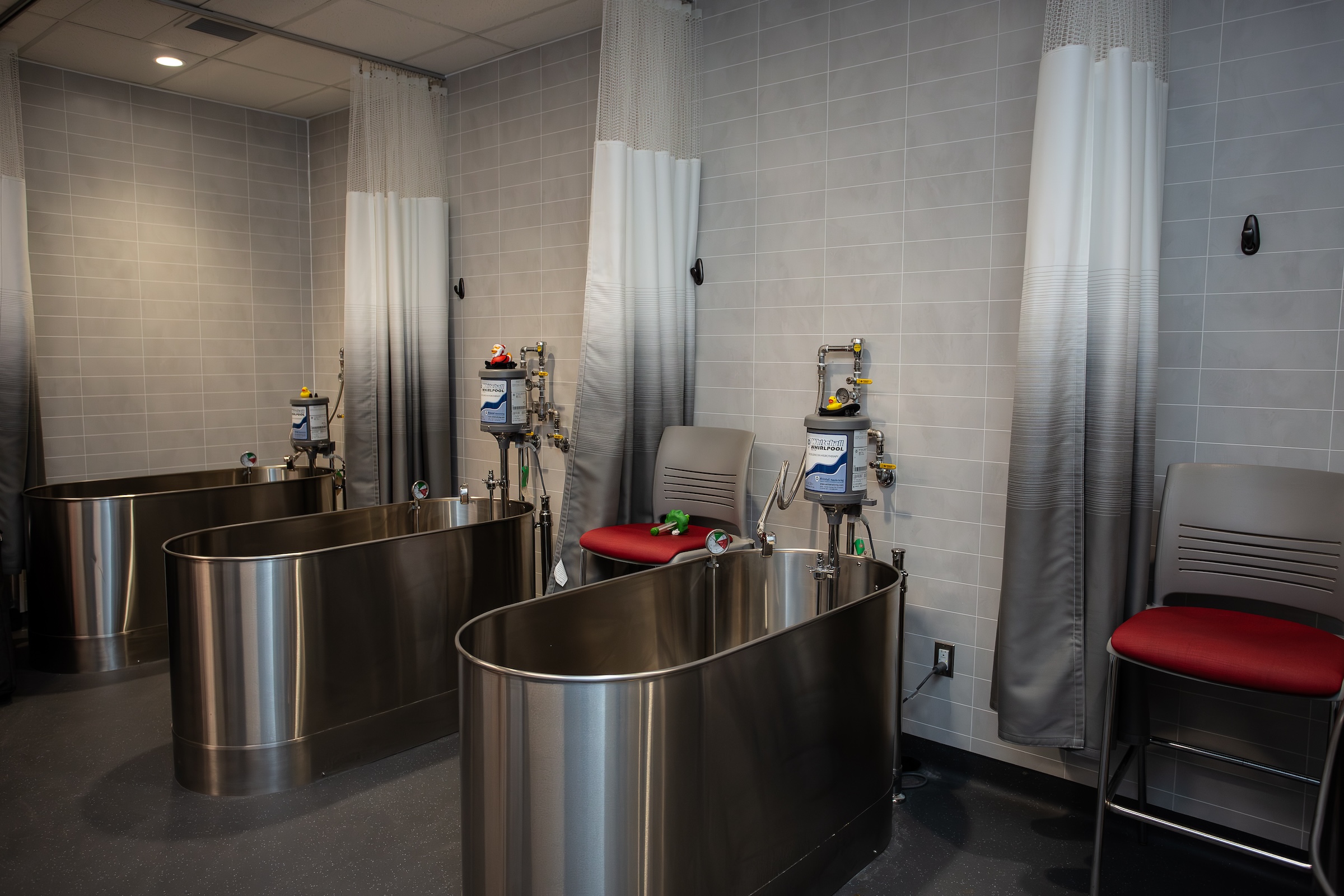 Three stainless steel tubs are shown with shower curtains in between and seats on either side.