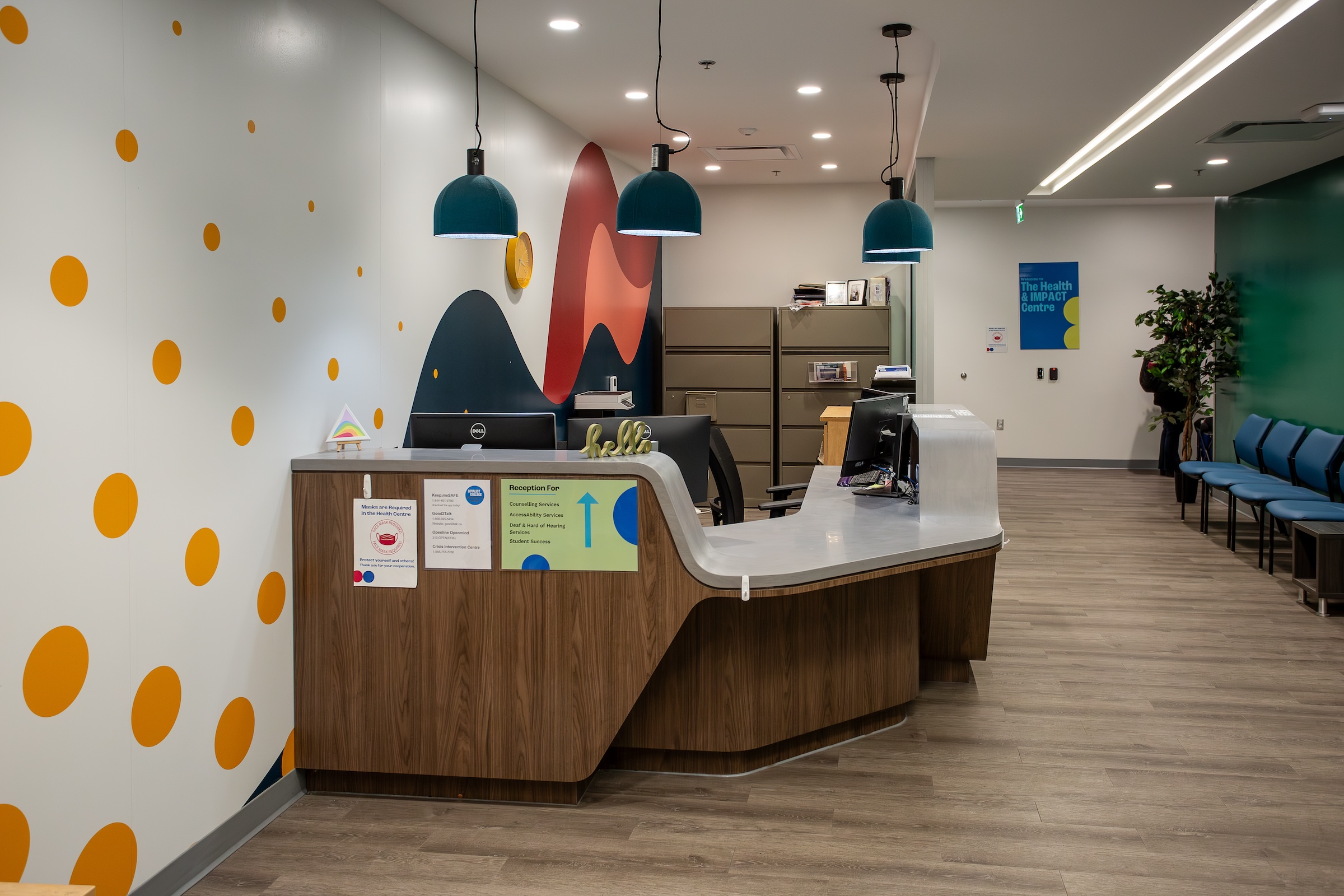 The Health and Impact Centre reception desk is shown. Empty chairs line the long room on the opposite side.