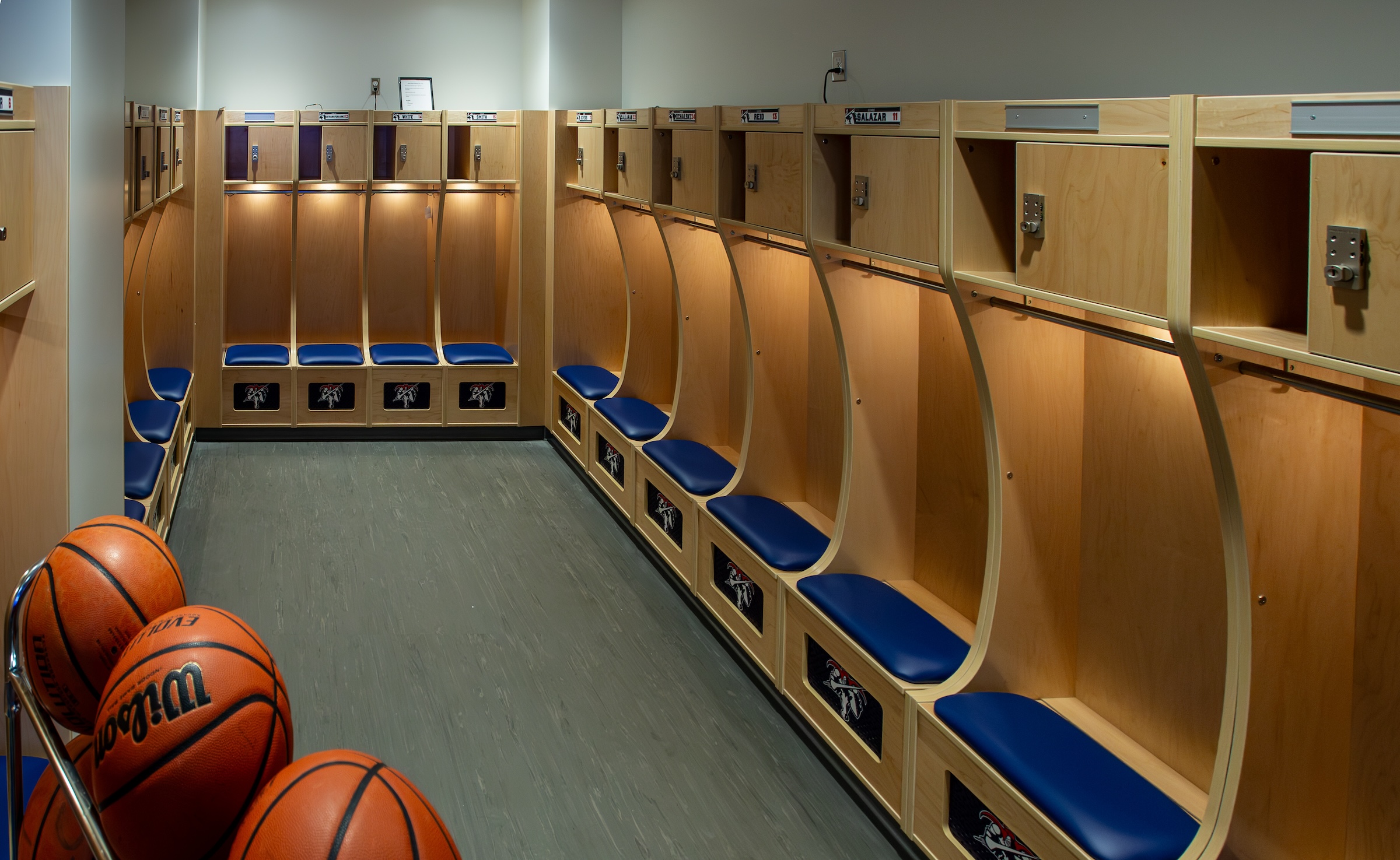 The Varsity Changeroom shows wood hangers and seats along the sides of the room with a rack of basketballs in the lower lefthand corner.