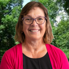 Loyalist College Student Advisor Mary McConnell smiles at the camera, sitting in front of a background of trees.