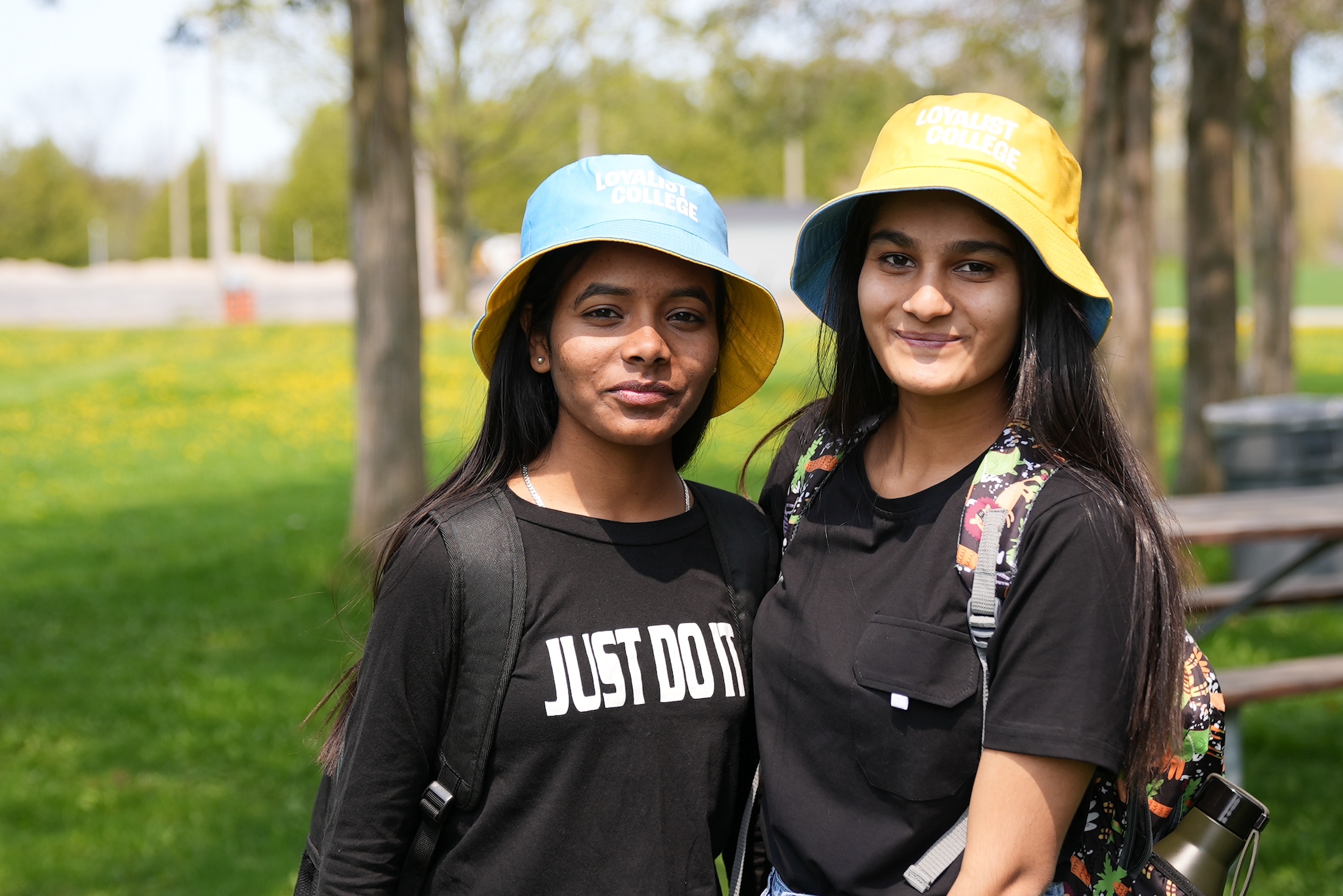 Two students smiling to the camera. The students are wearing black t-shirts and yellow and blue Loyalist College bucket hats.