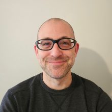 Loyalist College Student Advisor Cory Mestre smiles at the camera, sitting in front of a white background.