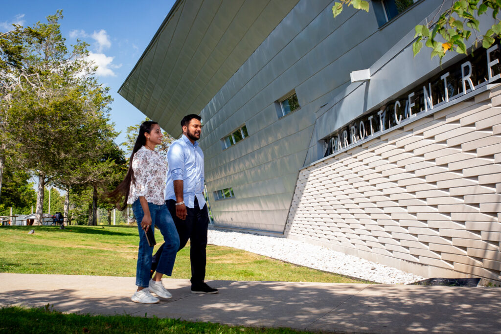 Two students walk side-by-side along a path outside the Parrott Centre Library on a sunny day.