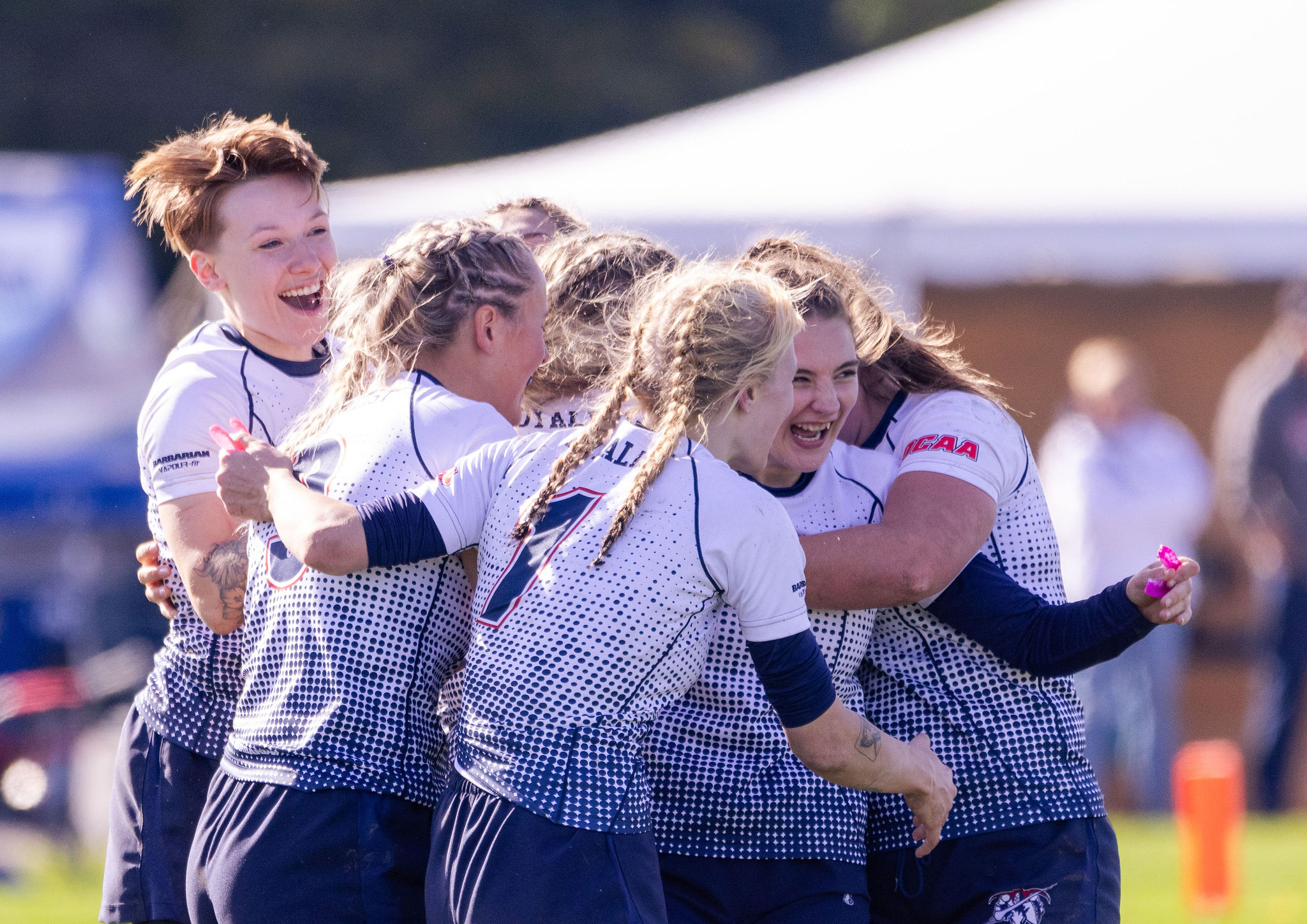 A group of rugby players celebrating together on the field, their faces beaming with joy and excitement after a successful play or victory. The team huddles in a tight embrace, showcasing their strong camaraderie and the intense emotions that come with the sport.