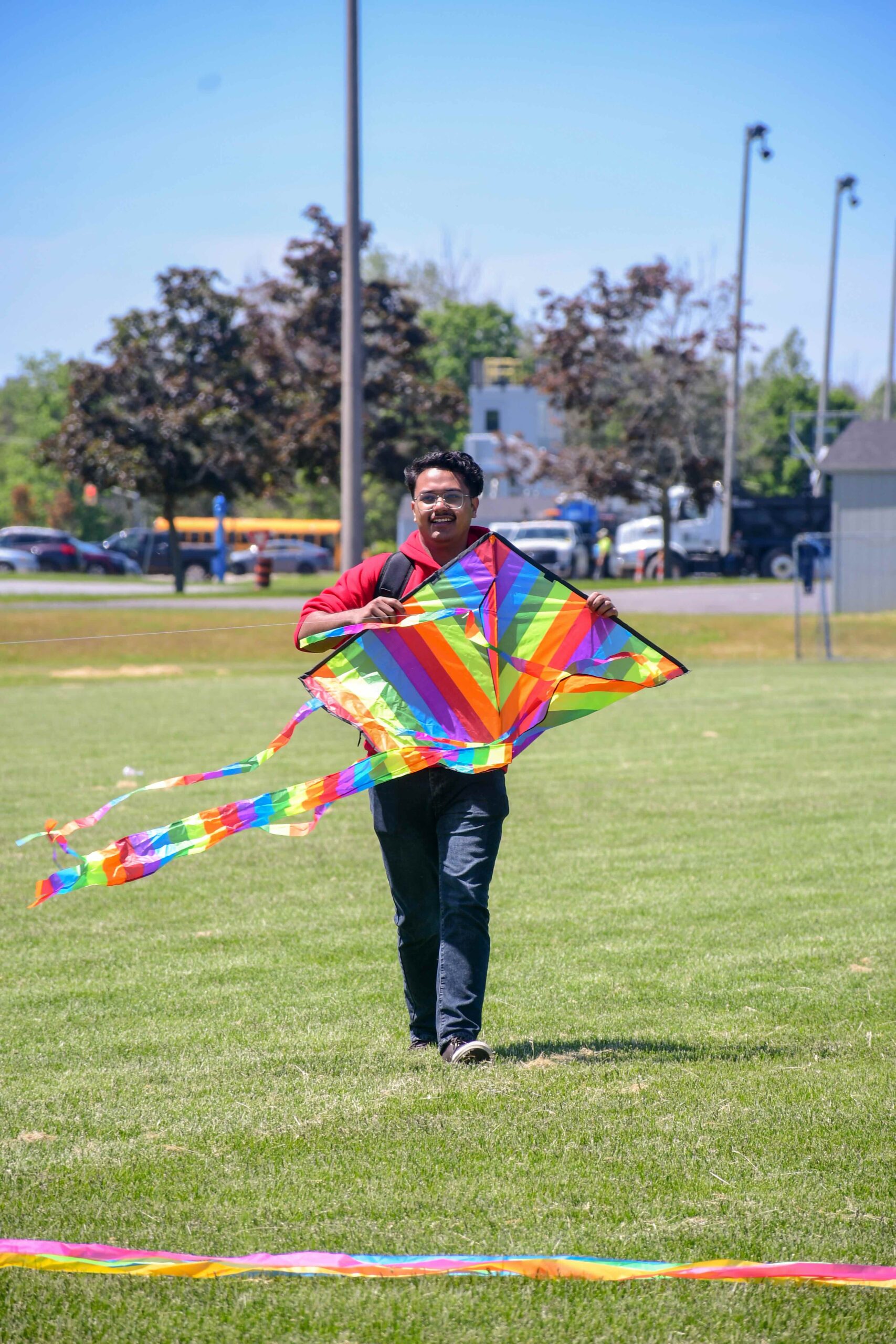 A student joyfully running across a field with a vibrant rainbow-colored kite, capturing the excitement and freedom of outdoor activities on campus.