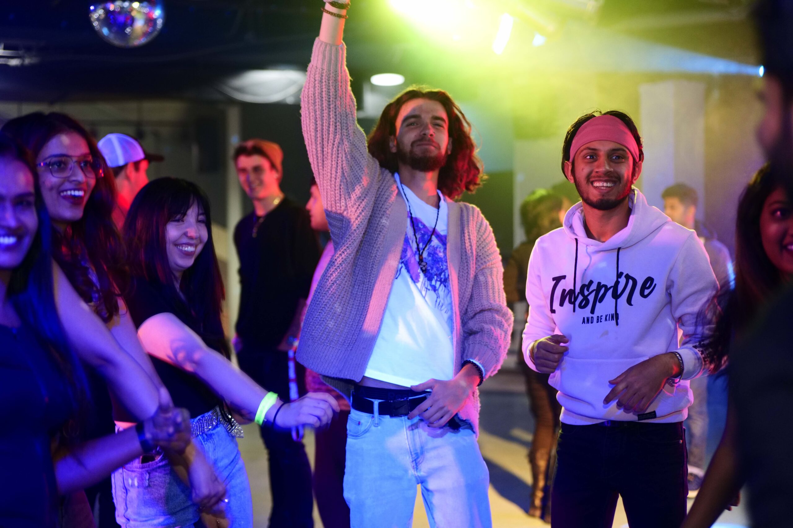 A lively group of students is captured dancing and enjoying themselves at a club or party event at Loyalist College. The colorful lighting and upbeat atmosphere set the stage for a night of fun and celebration. The students are smiling, laughing, and fully immersed in the moment, showcasing the vibrant social life on campus