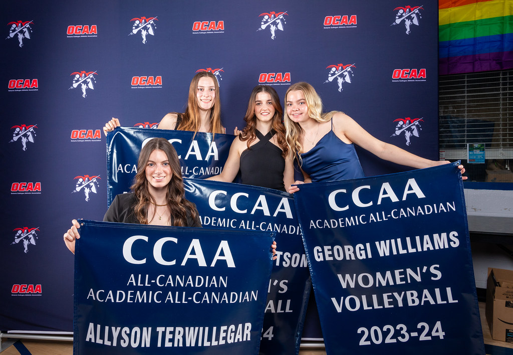 A group of Loyalist College students are holding CCAA Academic All-Canadian banners at the Ontario College Athletic Association awards ceremony. The student is standing in front of a navy background with OCAA logos.