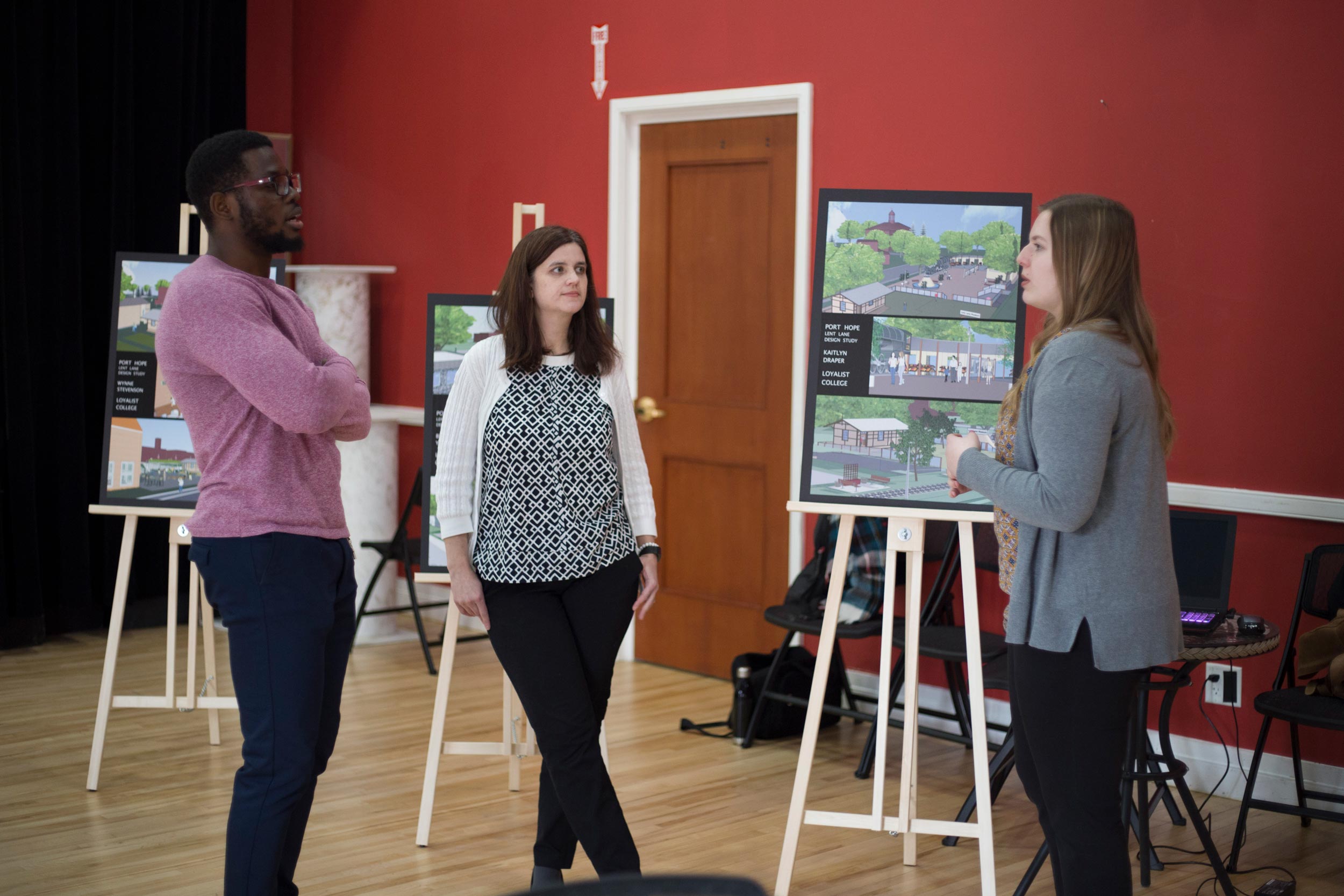 Students in the architectural technician program are presenting their projects in a room. The students are all wearing business attire and standing.