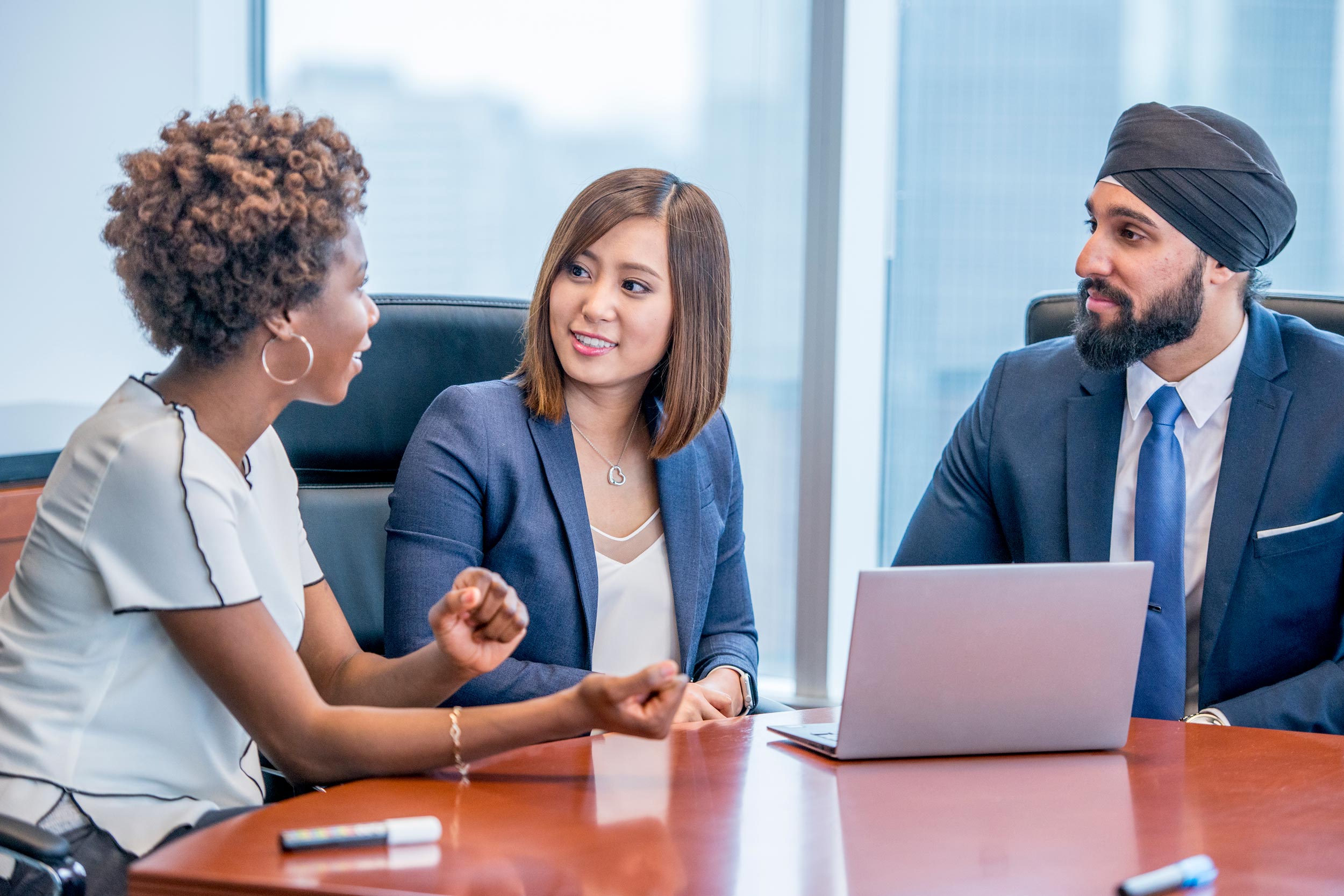 Three people are sitting down around a table engaged in a conversation.