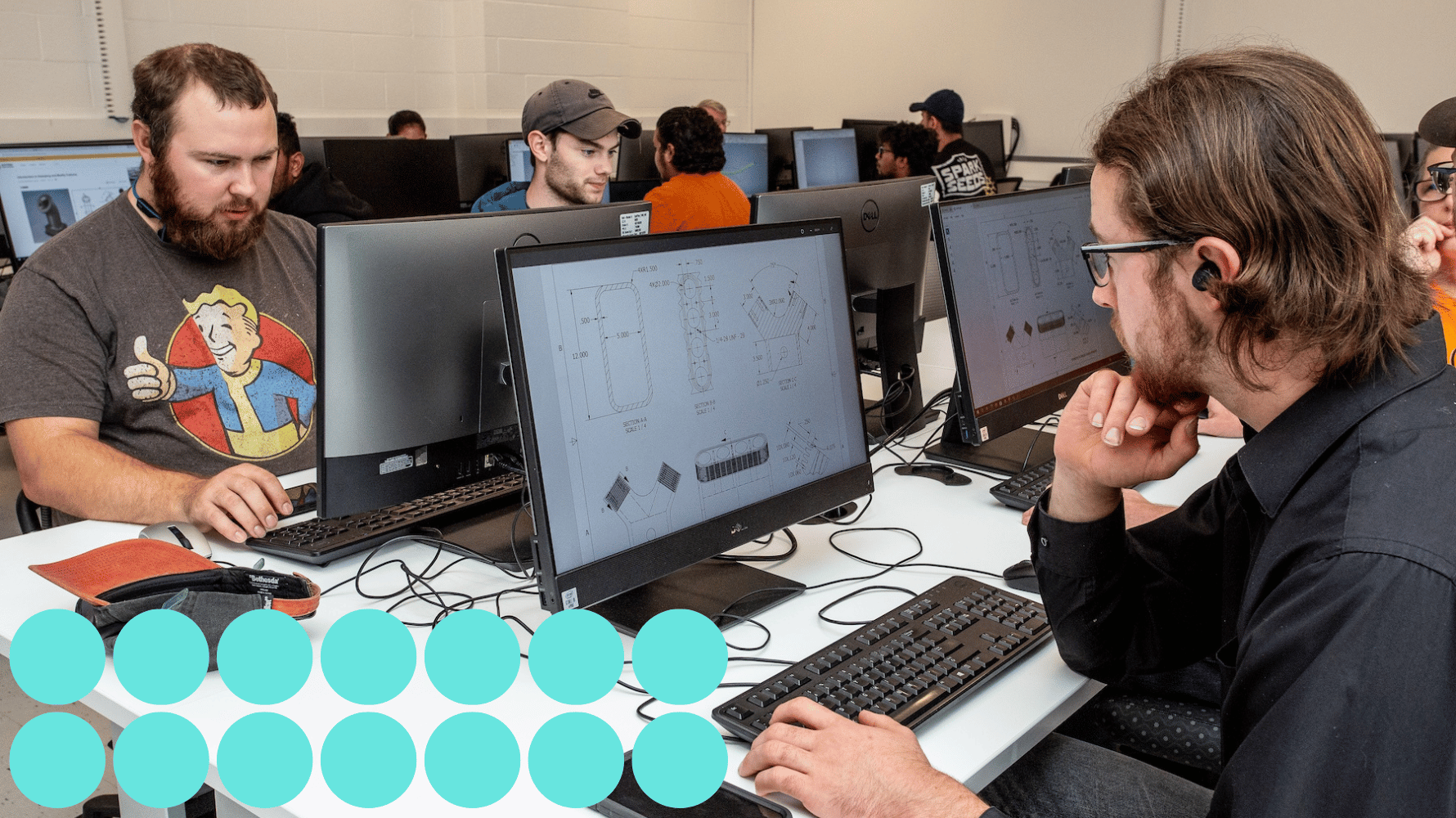 Students sit at workstations in a computer lab with engineering drawings of mechanical parts on their screens. Blue graphic circles are in the lower lefthand corner of the image.