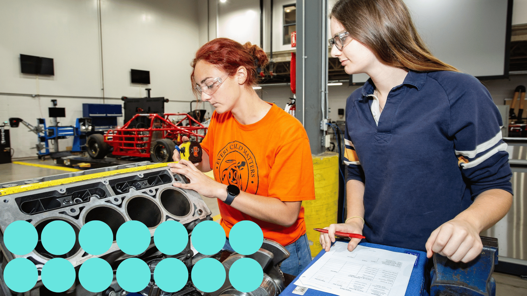 Two students in the Motive Power Fundamentals Parts and Counter Personnel program are working on a device while wearing safety goggles. They are focused on the task, handling tools in a hands-on learning environment. Fourteen blue graphic circles are in the lower lefthand corner of the image.