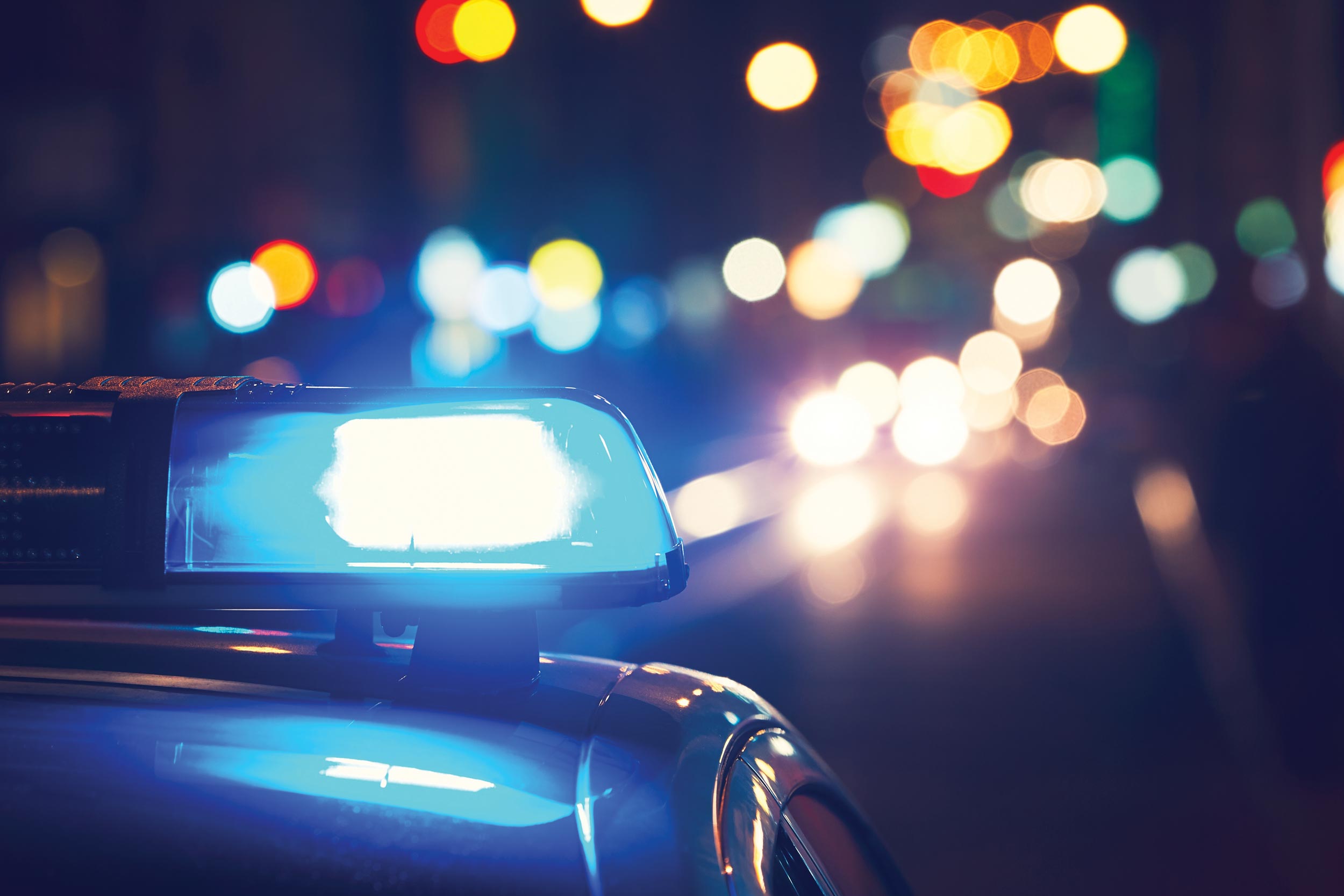 A close-up image of a police vehicle's light at night. There is bokeh lights shown in the background of the image.