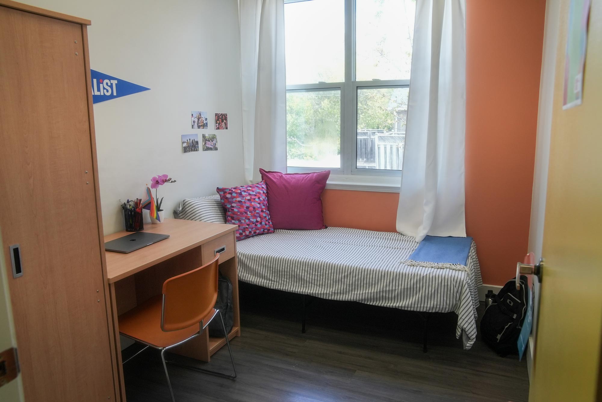 An interior picture of a dorm room at the Port Hope residence building. There is a closet, bed, window, desk and table.