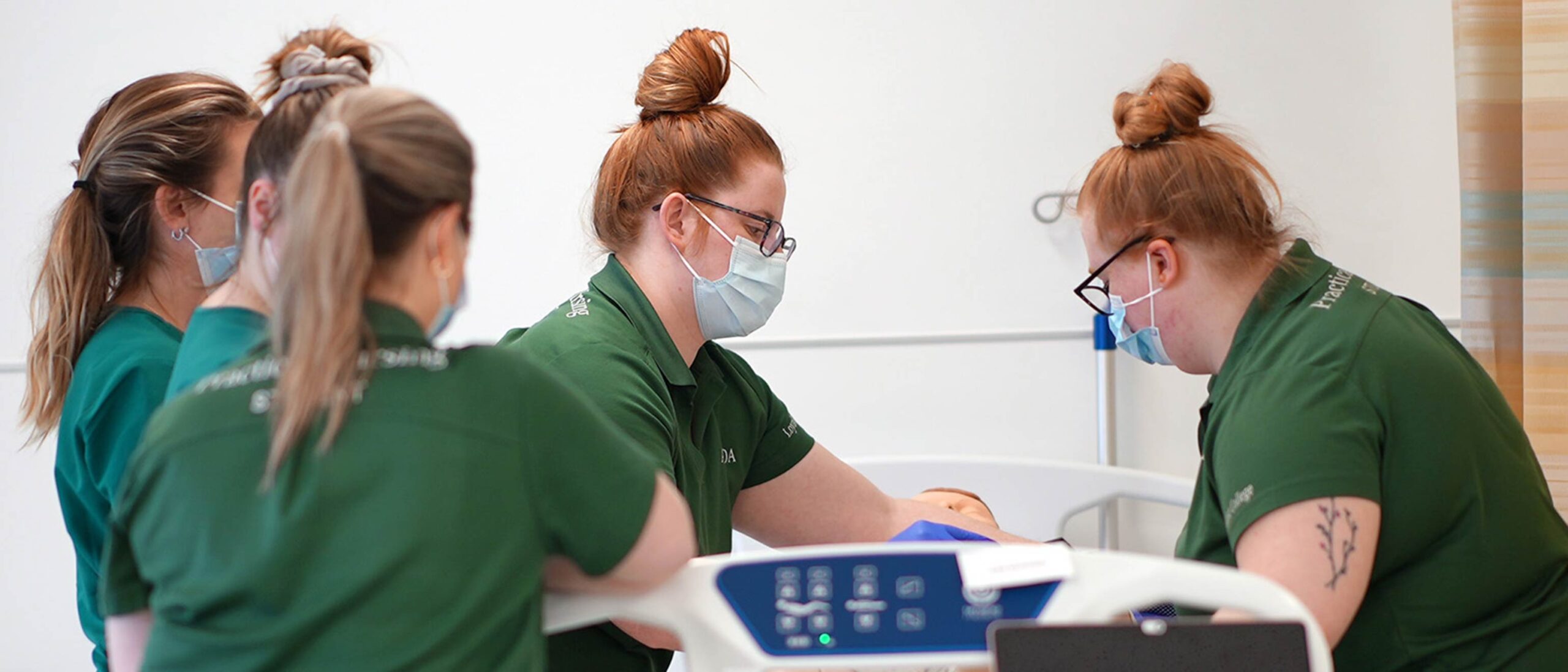 A group of five practical nursing students are working in a mock client setting with a fake body.