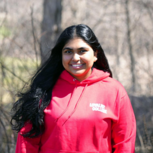 A headshot of Prashaani David Harris, a CYC student, wearing a red Loyalist sweater. In the background is a wooded forest in winter.