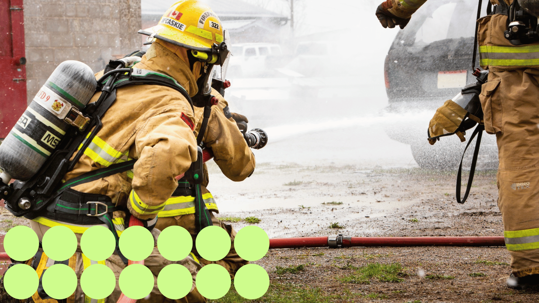 A group of students in the pre-service firefighter program are working on using gear and a hose to blow water onto a car outside. Fourteen green graphic circles are in the lower lefthand corner of the image.