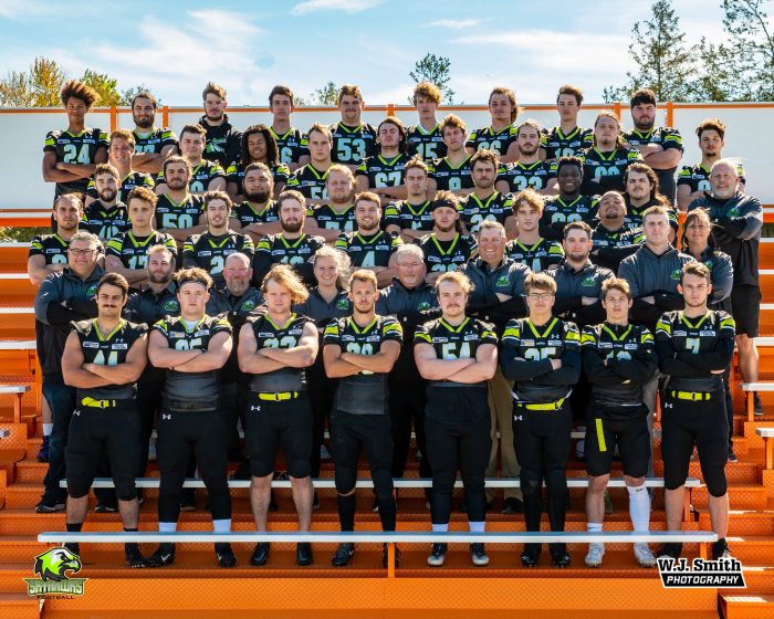 A team image of the Quinte Skyhawks in their uniforms. Team members and coaches stand on orange bleachers with arms crossed.