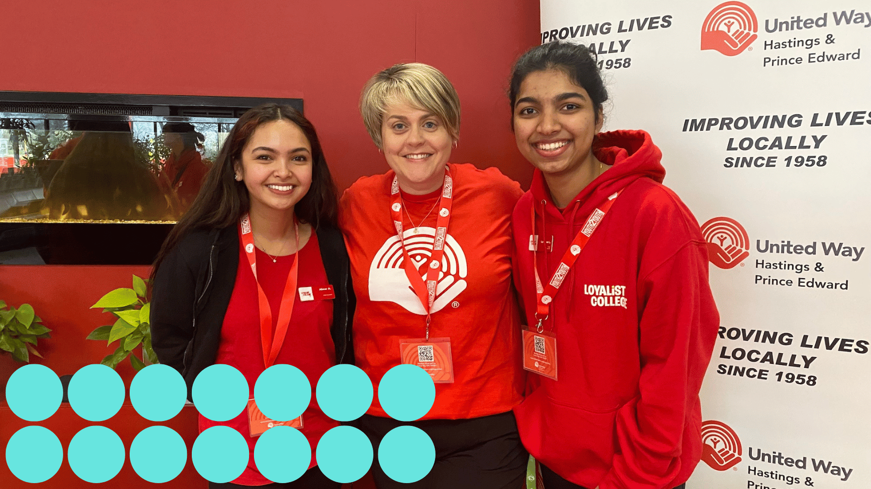 Two students stand on either side of a person wearing a United Way t-shirt. The banner in the background says "United Way, Hastings & Prince Edward, Improving Lives Locally since 1958." Blue graphic circles are in the lower lefthand corner of the image.