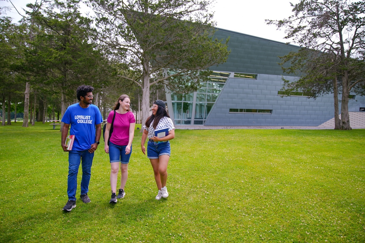 Three students holding books walk across the lawn with The Parrott Centre Library building in the background.