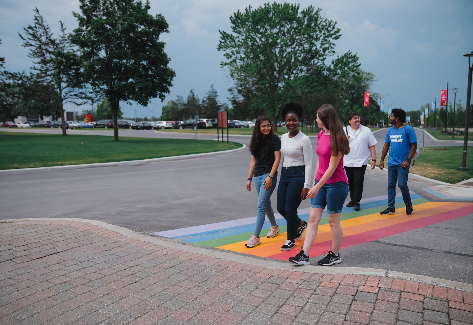 Five students are crossing a road talking to each other. The students are divided into two groups. One group has three students. The other group has two students.