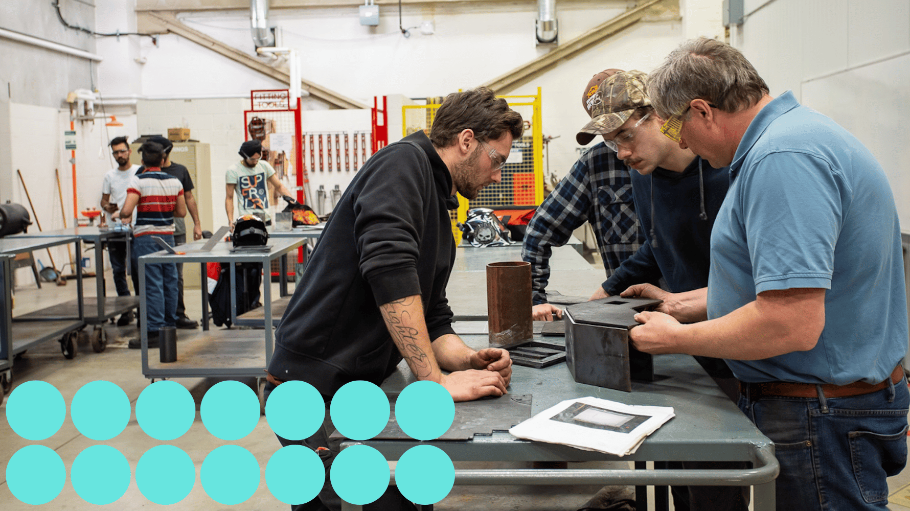 A professor places a metal piece on top of a base. Students watch, leaning over the metal work trolley in the lab. Blue graphic circles are in the lower lefthand corner of the image.