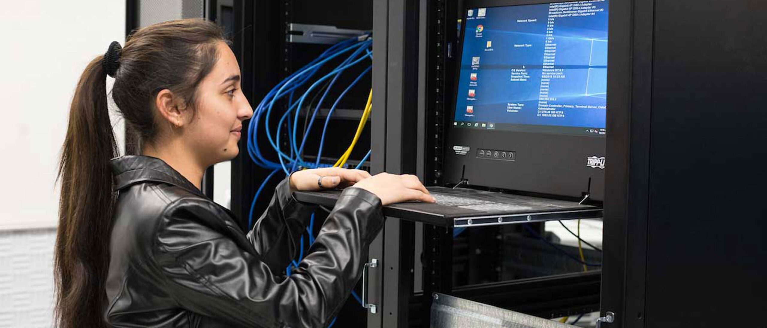 A student stands at a monitor and keyboard mounted to the back of a server rack.