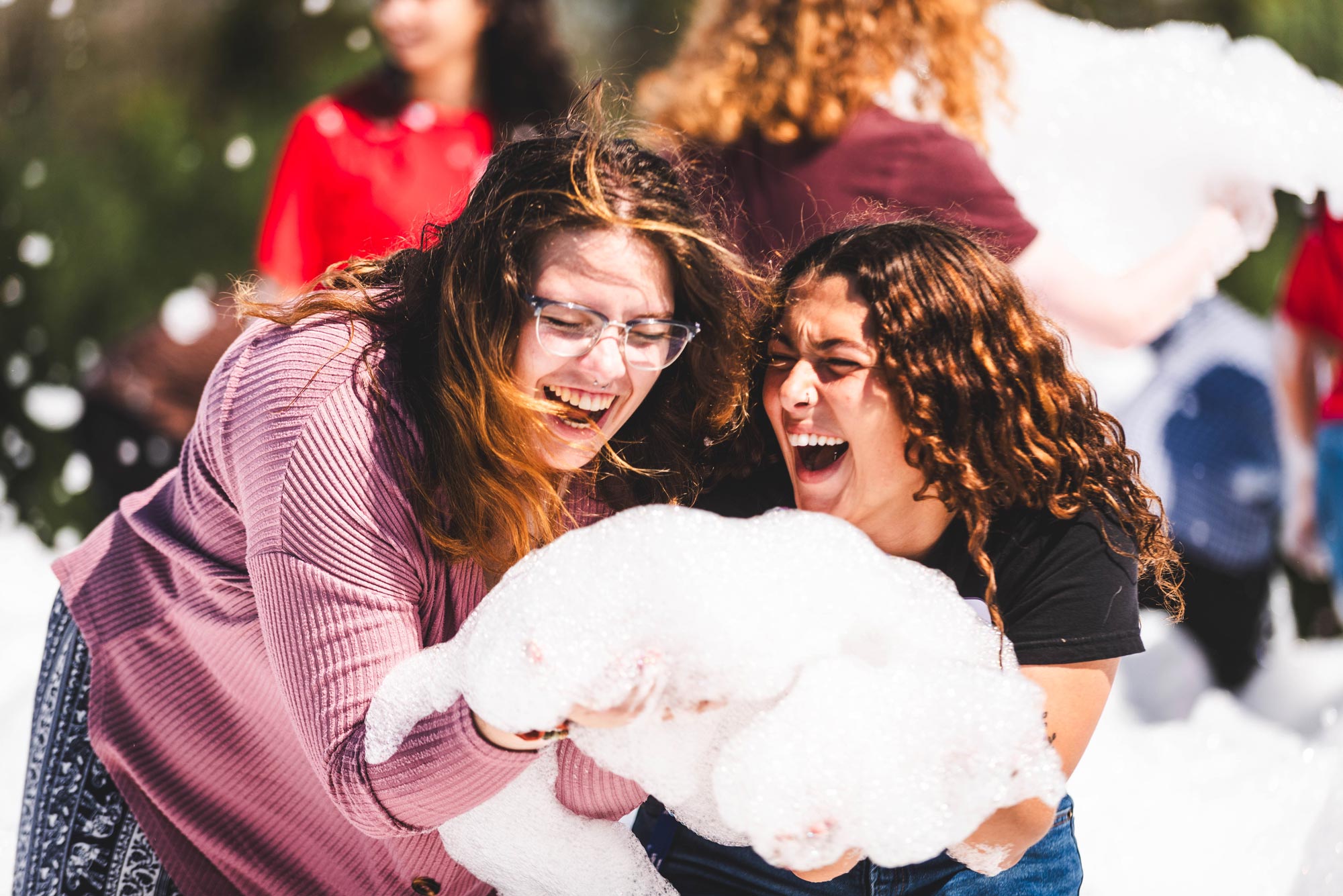 Two students outside on a sunny day laughing and holding foam.