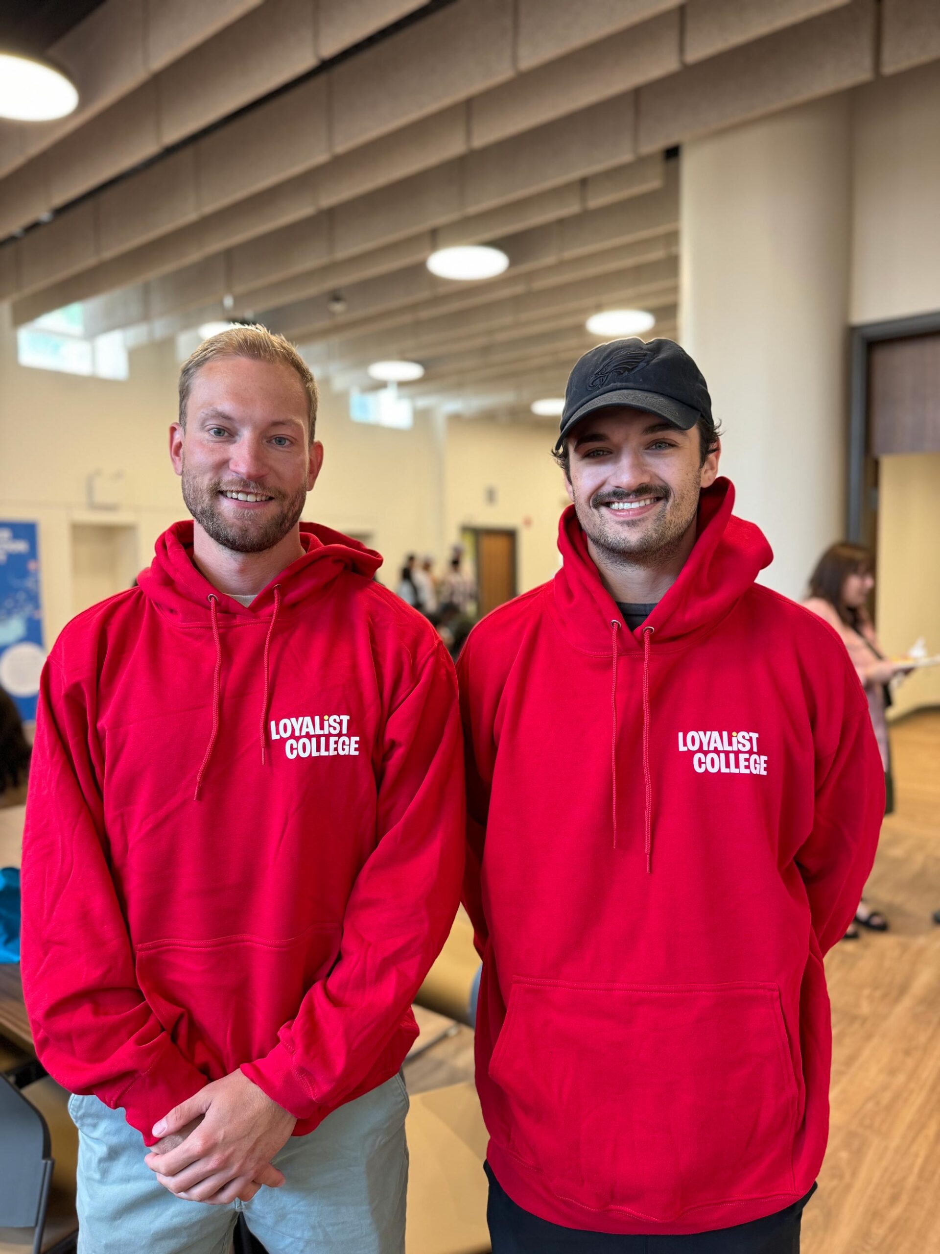 Two students smiling and wearing matching red Loyalist College hoodies.