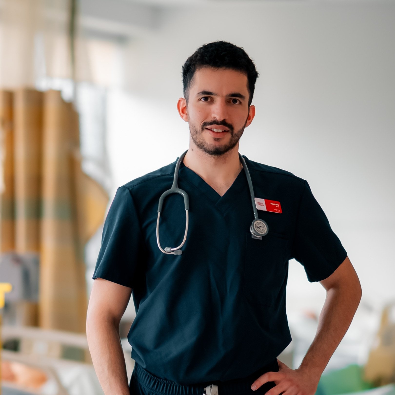 A headshot of Mustafa in the nursing wing, wearing dark blue scrubs.