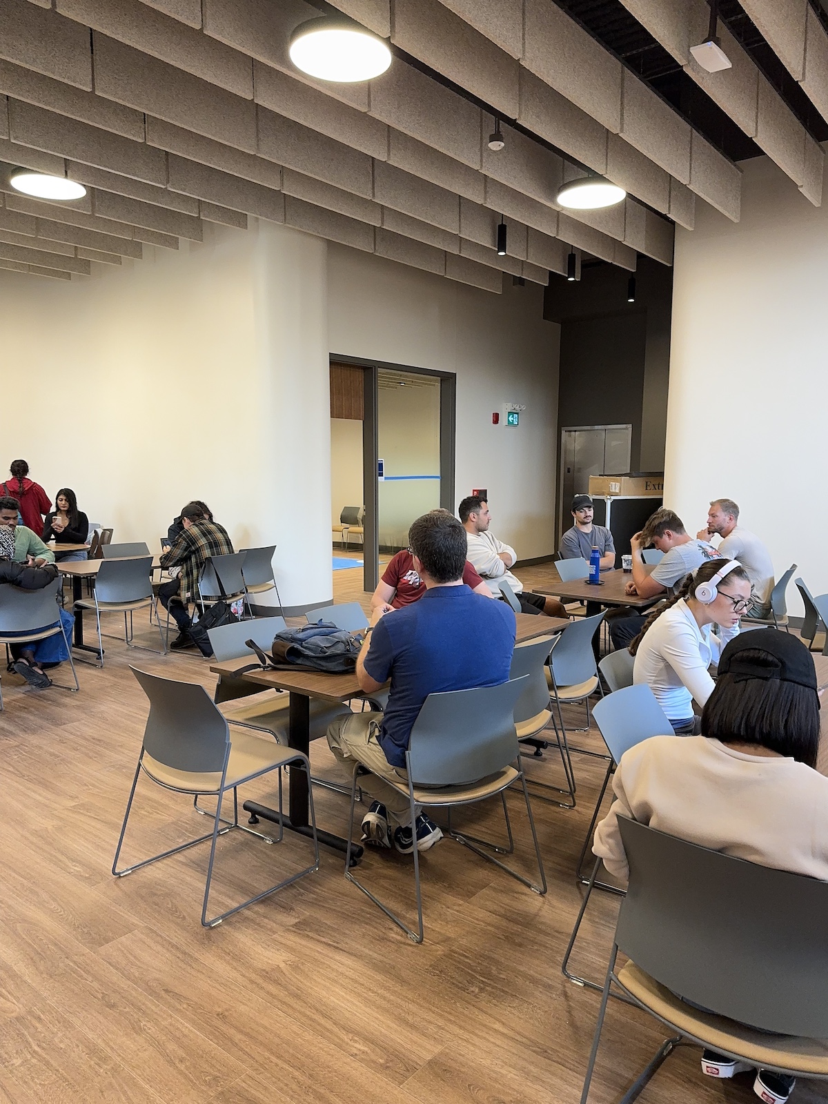 Students gathered in an open space, seated at tables in groups, at the Port Hope campus.