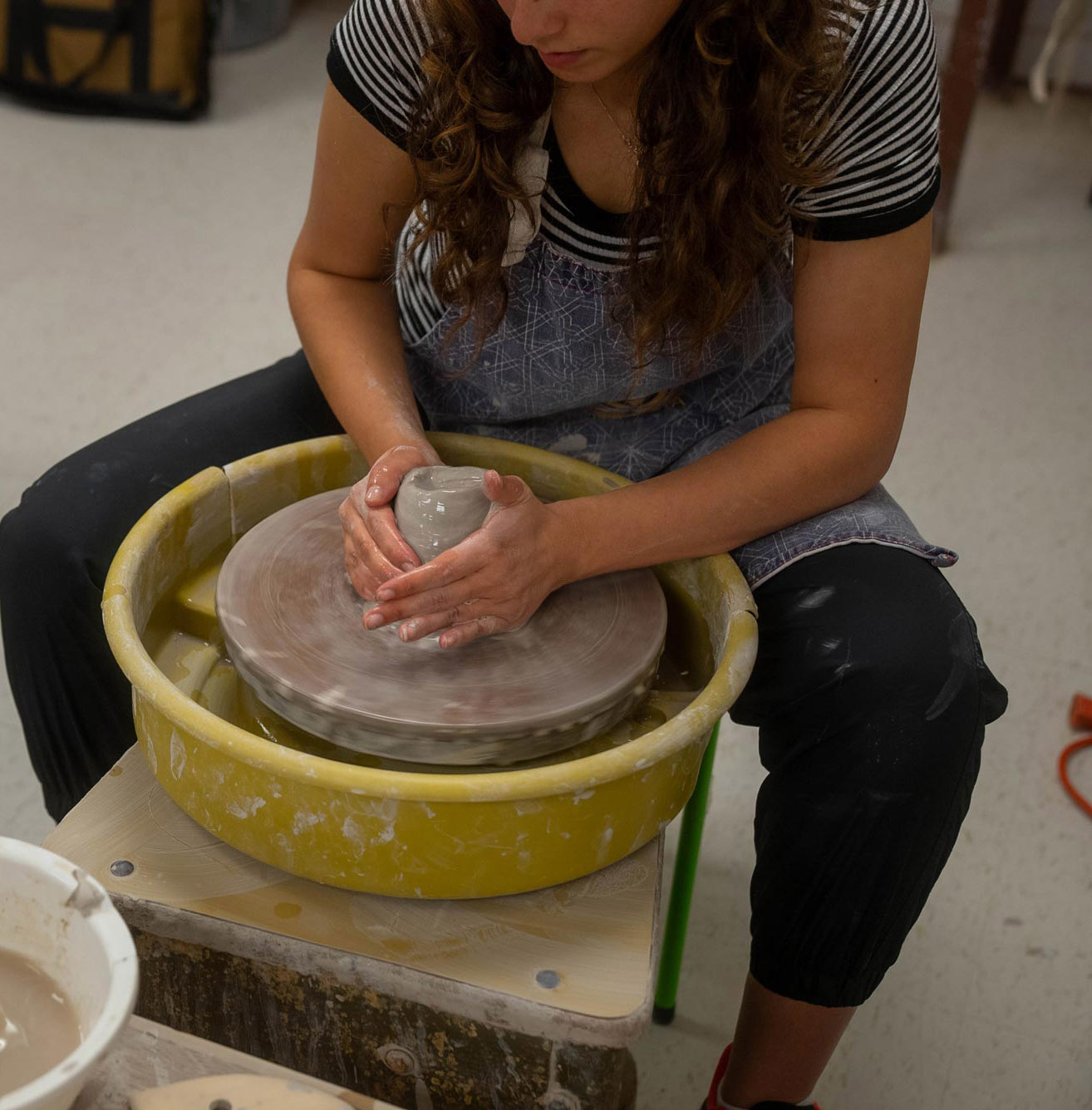 An individual works on a pottery wheel, shaping a clay object.