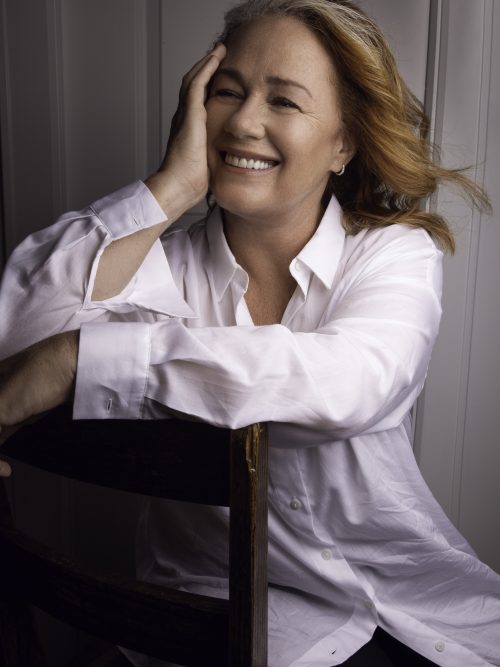 A headshot of Arlene Dickinson, smiling with her hand resting on the side of her face. The background is a white wood panelling.