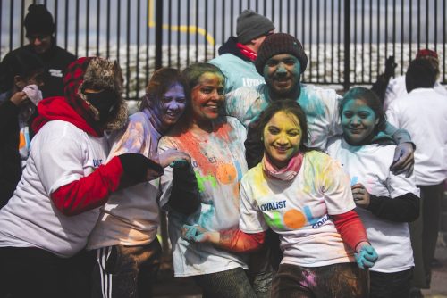 A group of Loyalist students smiling and covered in coloured powder, celebrating Holi.