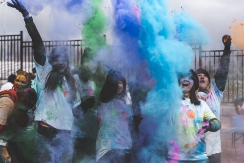 A group of Loyalist students throwing coloured powder in the air. Blue, green, and purple powder is clouded in front of the students.