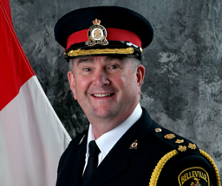 Headshot of Belleville Police Chief Michael Callaghan in his uniform in front of a grey background with a Canadian flag peeking in the left side of the frame.