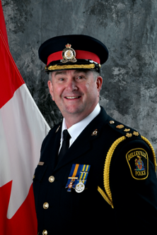 Headshot of Belleville Police Chief Michael Callaghan in his uniform in front of a grey background with a Canadian flag peeking in the left side of the frame.