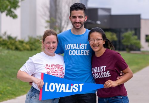 Three students stand side-by-side, smiling and holding a blue Loyalist banner.