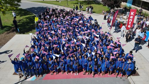 Drone shot of Loyalist graduates in blue graduation gowns out front of the college.