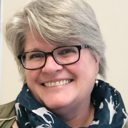 A close up headshot of Shannon Claggett, Dean of Applied Sciences, Skills and Technology, wearing a scarf and classes, smiling.