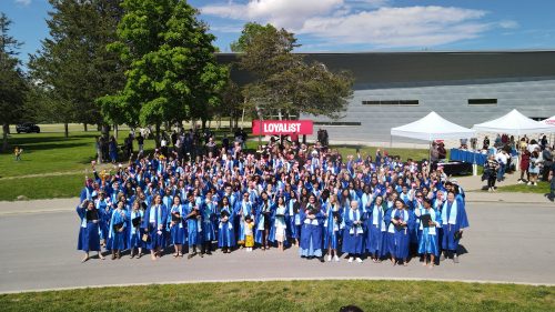 A drone shot of a group of Loyalist College graduates standing outside smiling at their convocation ceremony.