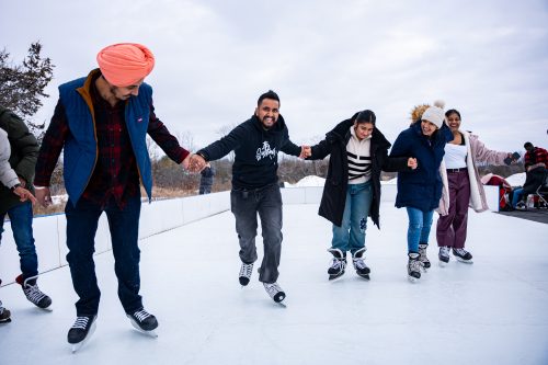 A group of students wearing skates, holding hands and skating on ice.