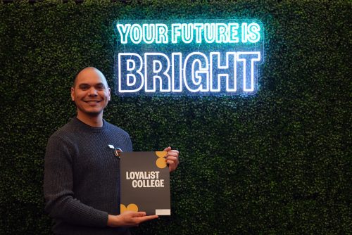 A Loyalist student posing with an awards envelope in front of a neon sign that says "Your Future is Bright".