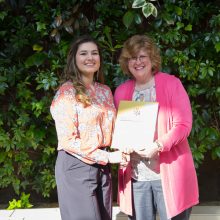 Natasha Mathieu, a Loyalist Biotechnology student, is presented with an award by Dr. Ann Marie Vaughan, President and CEO. They're standing in front of a live greenery wall in the Loyalist Link Lounge.