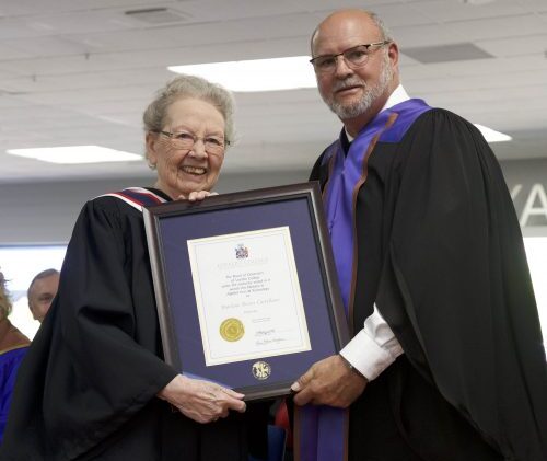 Dr. Marlene Brant Castellano being presented with an Honorary Diploma by Bob Forder, Chair of the Loyalist College Board of Governors. Both are wearing ceremonial graduate gowns.