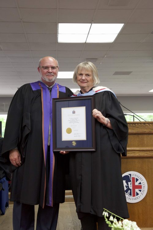 Bob Forder, Chair of the Loyalist College Board of Governors, being presented with an Honorary Diploma by June Hagerman, Past Chair, Loyalist College Board of Governors. They're standing in front of a podium.