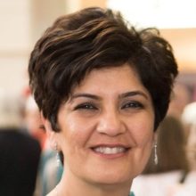 A headshot of Dr. Karima Velji, smiling in front of a blurred background.